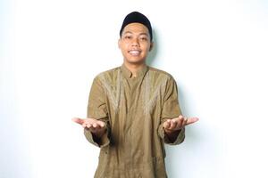 sorridente asiatico musulmano uomo indossare islamico vestito presentazione con Aperto palma a telecamera isolato su bianca sfondo foto