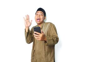divertente asiatico musulmano uomo indossare islamico vestito Tenere mobile Telefono raccolta mano sembra sorpreso isolato su bianca sfondo foto