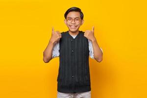 ritratto di allegro giovane uomo asiatico che mostra i pollici in su o segno di approvazione isolato su sfondo giallo foto