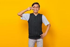 ritratto di allegro giovane uomo asiatico che fa segno di pace con le dita su sfondo giallo foto