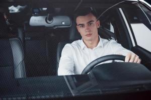un giovane siede in un'auto appena acquistata tenendo le mani su un timone foto