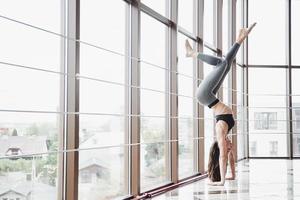 una sportiva sportiva che sta facendo lezioni di yoga, allungando le gambe vicino alla grande finestra foto