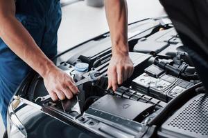 le mani del meccanico controllano la funzionalità dell'auto nel cofano aperto, primo piano. foto