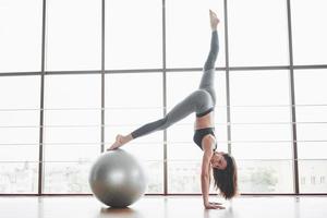 sport è una bella donna che sta facendo lezioni di yoga, allungando le gambe sulla palla vicino alla grande finestra foto