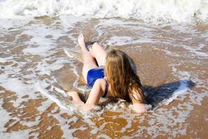 ragazza nel un' blu bagnarsi completo da uomo bugie su il riva del mare e rilassa. onde carezza il ragazze corpo foto