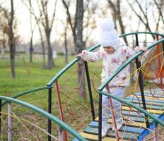 poco ragazza è giocando su il terreno di gioco nel il parco. il bambino va su il passaggi di il terreno di gioco. foto