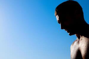 silhouette di un' uomo contro un' blu cielo e sole. un' uomo nel gocce di mare acqua foto