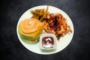 hamburger con pollo taglio, francese patatine fritte, e salsa su un' bianca piatto su un' nero sfondo foto