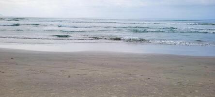 Immagine di spiaggia con bianca sabbia e calma mare su soleggiato giorno con bagnanti e surfers su il spiaggia foto