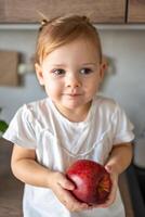 bambino ragazza bionda mangiare un Mela nel il cucina, concetto di salutare cibo per bambini foto