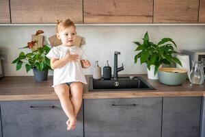 un' bambino ragazza con un' fiore su il cucina tavolo avendo divertimento foto