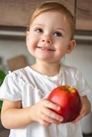 bambino ragazza bionda mangiare un Mela nel il cucina, concetto di salutare cibo per bambini foto