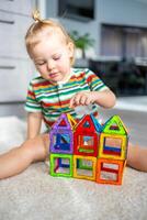 poco ragazza giocando colorato magnete plastica blocchi kit a casa. il bambino giocando educativo Giochi. presto infanzia sviluppo. foto