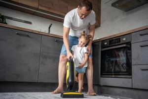 padre e figlia avendo divertimento con vuoto addetto alle pulizie mentre pulizia a casa cucina foto