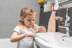 contento bambino piccolo ragazza spazzolatura denti nel il bagno foto