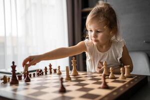 poco ragazza giocando scacchi a il tavolo nel casa cucina. il concetto presto infanzia sviluppo e formazione scolastica. famiglia tempo libero, comunicazione e ricreazione. foto