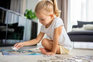 poco bionda ragazza si siede a casa su il tappeto e raccoglie puzzle foto