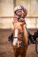 poco bambino equitazione lezione. tre anni ragazza cavalcate un' pony e fa esercizi foto