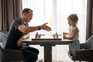 padre insegnamento il suo poco figlia per giocare scacchi a il tavolo nel casa cucina. il concetto presto infanzia sviluppo e formazione scolastica. famiglia tempo libero, comunicazione e ricreazione. foto