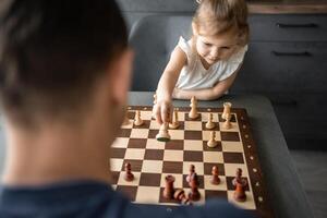 poco ragazza giocando scacchi con sua padre a il tavolo nel casa cucina. il concetto presto infanzia sviluppo e formazione scolastica. famiglia tempo libero, comunicazione e ricreazione. foto