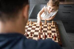 padre insegnamento il suo poco figlia per giocare scacchi a il tavolo nel casa cucina. il concetto presto infanzia sviluppo e formazione scolastica. famiglia tempo libero, comunicazione e ricreazione. foto