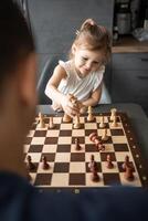 padre insegnamento il suo poco figlia per giocare scacchi a il tavolo nel casa cucina. il concetto presto infanzia sviluppo e formazione scolastica. famiglia tempo libero, comunicazione e ricreazione. foto