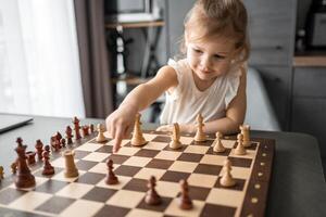 poco ragazza giocando scacchi a il tavolo nel casa cucina. il concetto presto infanzia sviluppo e formazione scolastica. famiglia tempo libero, comunicazione e ricreazione. foto