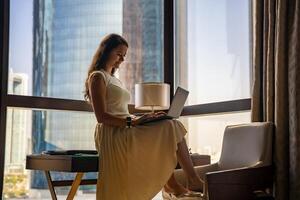 elegante donna d'affari libero professionista Lavorando con il computer portatile e lei è seduta su il tavolo, godendo panoramico Visualizza nel il città sfondo. Basso chiave foto. alto qualità foto