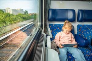 bellissimo poco ragazza utilizzando digitale tavoletta durante in viaggio di ferrovia nel Germania, Europa foto
