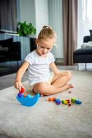 poco ragazza giocando con di legno equilibratura giocattolo su il pavimento nel casa vivente camera. foto