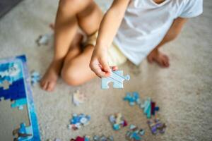 puzzle pezzo nel bambino mano. poco ragazza si siede a casa su il tappeto e raccoglie puzzle foto