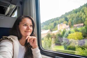 giovane donna guardare attraverso il treno finestra. contento treno passeggeri in viaggio e guardare attraverso il finestra, Europa foto