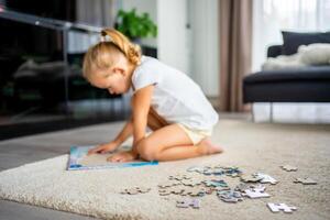 poco bionda ragazza si siede a casa su il tappeto e raccoglie puzzle foto