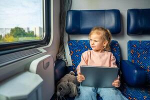 poco ragazza utilizzando digitale tavoletta durante in viaggio di ferrovia nel Europa foto