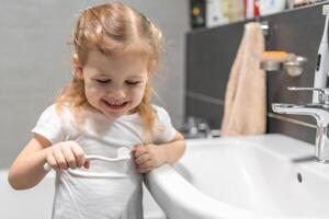 contento bambino piccolo ragazza spazzolatura denti nel il bagno foto