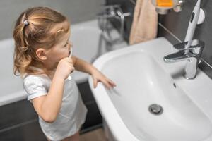 contento bambino piccolo ragazza spazzolatura denti nel il bagno foto
