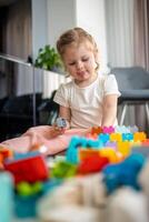 poco ragazza giocare con costruttore giocattolo su pavimento nel casa, educativo gioco, la spesa tempo libero attività tempo concetto foto