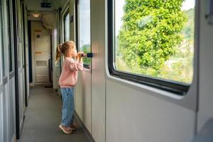 carino poco ragazza guardare su treno finestra fuori, mentre esso in movimento. in viaggio di ferrovia nel Europa foto