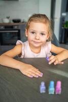 ritratto di poco ragazza fare manicure e pittura Chiodi con colorato rosa, blu e viola chiodo polacco a casa. foto