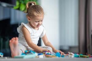 concentrato poco ragazza giocando con piccolo costruttore giocattolo su il pavimento nel casa vivente camera, educativo gioco, la spesa tempo libero attività tempo concetto foto