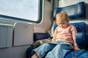carino poco ragazza utilizzando digitale tavoletta durante in viaggio di ferrovia, Europa foto
