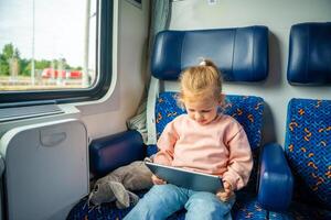 poco ragazza utilizzando digitale tavoletta durante in viaggio di ferrovia, Europa foto