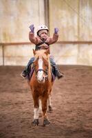 poco bambino equitazione lezione. tre anni ragazza cavalcate un' pony e fa esercizi. alto qualità foto