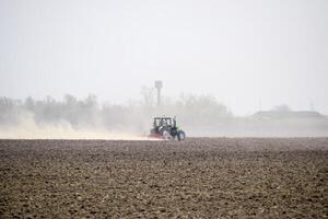 il trattore erpici il suolo su il campo e crea un' nube di polvere dietro a esso foto