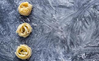 crudo tagliatelle nido su il spolverata di farina nero di legno sfondo foto