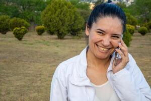 latino donna utilizzando sua cellula Telefono nel un' parco. foto