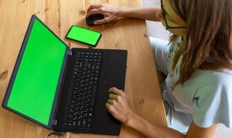 superiore Visualizza giovane ragazza Lavorando o studiando utilizzando sua il computer portatile e smartphone con finto su verde schermi. foto