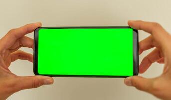 femmina mani siamo Tenere smartphone con verde schermo finto su su neutro beige sfondo morbido messa a fuoco foto