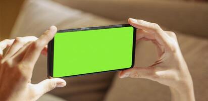 vicino su di mani di dire bugie a divano donna Tenere smartphone con verde schermo su sfocato sfondo. foto