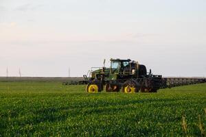 trattore con il Aiuto di un' spruzzatore spray liquido fertilizzanti su giovane Grano nel il campo. foto